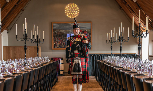 Piper in the Jacobite Room with long tables dressed for a pre-tattoo dinner