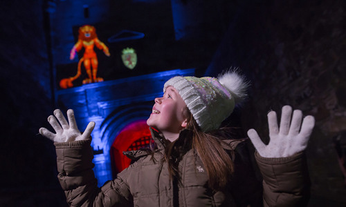 Photo shoot for Castle of Light with girl looking at the light projection at the entrance to Edinburgh Castleel