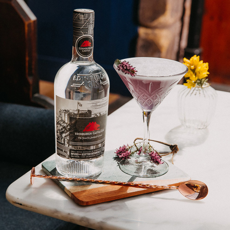 Bottle of Edinburgh Castle Gin on a table with a stirrer and cocktail in a martini glass