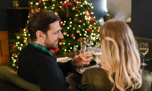 Man and woman sitting by a Christmas tree in the Queen Anne Room at Edinburgh Castle clinking wine glasses