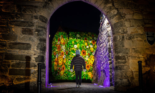 A child walking through an brick archway towards a light display being projected onto a wall