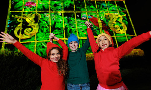 three children with their hands in the air and light projection on a wall behind them