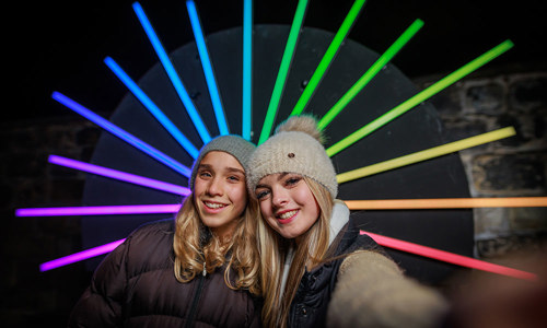 Two young ladies with a light projection on a wall behind them