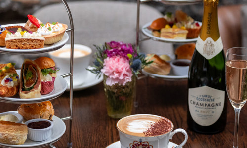 A cake stand full of sumptuous sweet and savoury treats with rosé Champagne and a latte served in a bone china cup and saucer