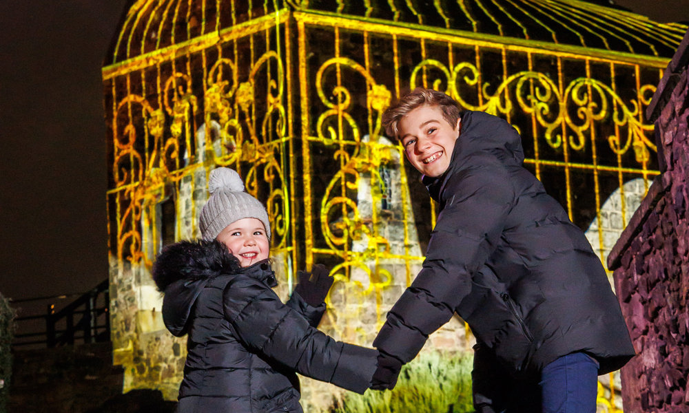 Two children holding hands smiling and walking towards a lit up building