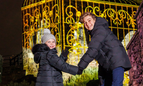 Two children holding hands smiling and walking towards a lit up building