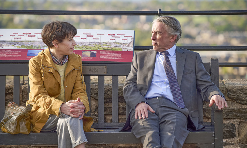 Left to right, actors Sally Hawkins & Steve Coogan sitting on a bench, with Edinburgh city centre in the background