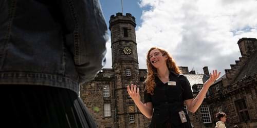 A lady in black and white uniform standing in Crown Square at Edinburgh Castle wearing a portable wireless receiver and headset