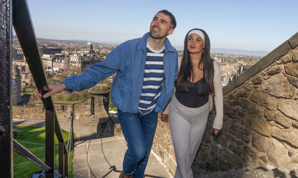 Two people walking up a set of stairs under bright blue skies and a city view in the background