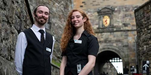 Two people in black and white uniform standing in the entrance to Edinburgh Castle wearing portable wireless receiver and headset