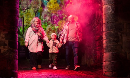 A family with a small child walking through the lit up portcullis at the castle