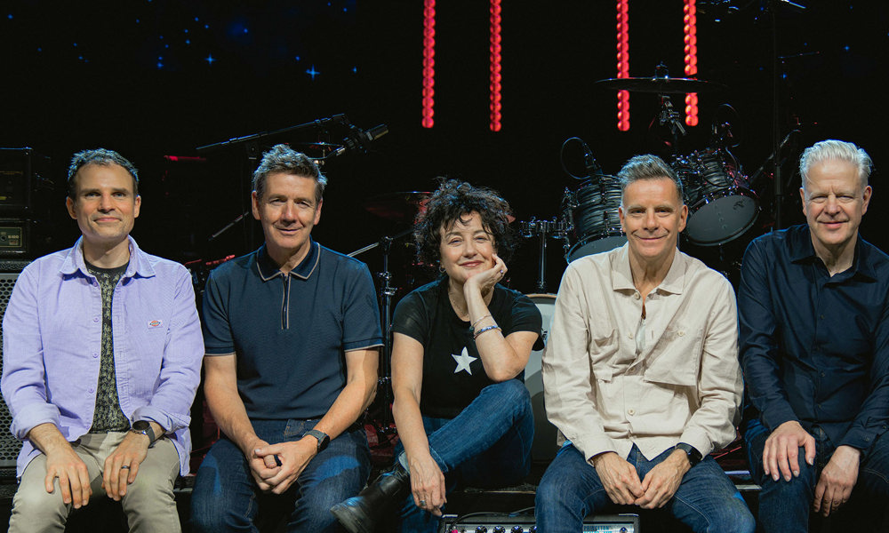 Deacon Blue band members sitting in a line on the edge of a stage