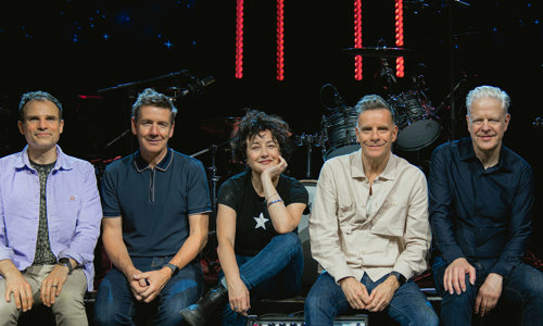 Deacon Blue band members sitting in a line on the edge of a stage