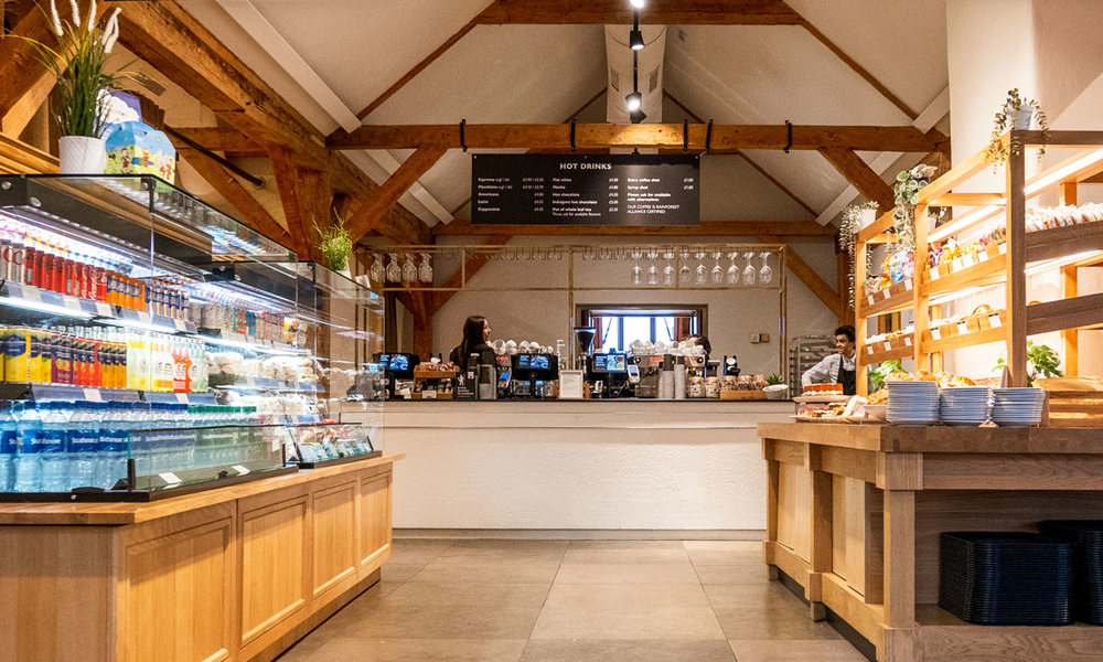 A fresh and bright café with a cooler cabinet filled with a variety of drinks and a beautiful cake display with tempting sweet and savoury treats