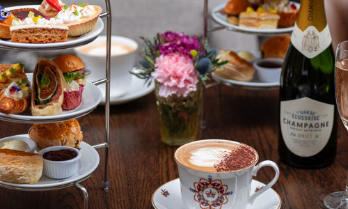 A cake stand full of sumptuous sweet and savoury treats with rosé Champagne and a latte served in a bone china cup and saucer