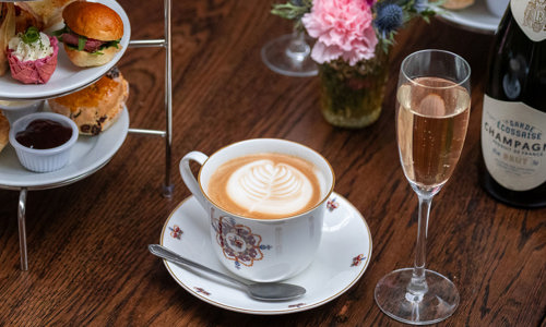 A cake stand full of sumptuous sweet and savoury treats with rosé Champagne and a latte served in a bone china cup and saucer